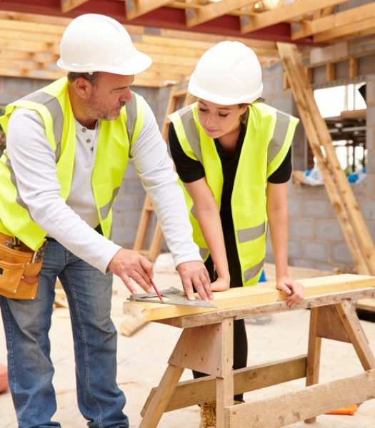 Carpenter With Female Apprentice Working On Building Site